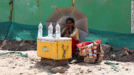 Девојка која продаје воду користи кишобран да би се заштитила од сунчевих зрака у Њу Делхију.