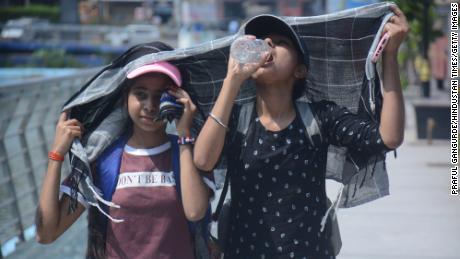 Девојке покривају главе док шетају и пију воду на ужареној поподневној врућини Мумбаија.
