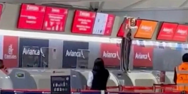 Остали путници на аеродрому могу издалека да виде особу ван контроле – како стоји на шалтеру за пријаву и држи екран изнад њега.